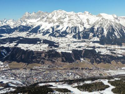 Am oberen Bildrand das Dachsteinmassiv, Bildmitte die Gemeinde Ramsau am Dachstein und unten, im Ennstal, die Stadt Schladming; der Blick geht von Süden nach Norden.